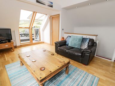 A living room with a brown leather sofa cushions wooden coffee table a rug and a television at Bwthyn Awel in Church Bay near Cemaes Bay