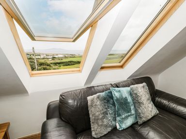 A black leather sofa with three cushions under slanted skylight windows showing a rural landscape at Bwthyn Awel Church Bay near Cemaes Bay