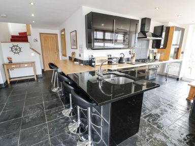 A kitchen with black countertops and bar stools at Bwthyn Awel in Church Bay near Cemaes Bay