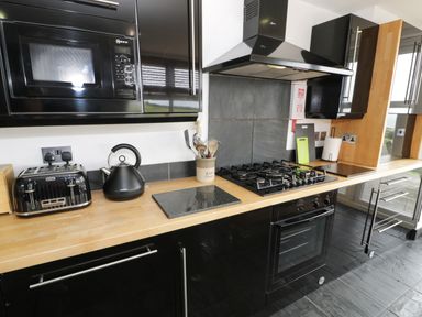 A kitchen with black cabinets a wooden countertop a microwave toaster kettle gas stove and oven at Bwthyn Awel in Church Bay near Cemaes Bay