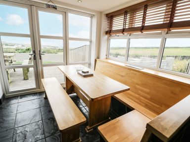 A dining area with wooden table and benches next to windows showing outdoor view at Bwthyn Awel in Church Bay near Cemaes Bay
