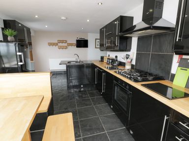 A kitchen with black cabinets wooden countertops a gas stove a sink a wooden dining bench and table at Bwthyn Awel in Church Bay near Cemaes Bay