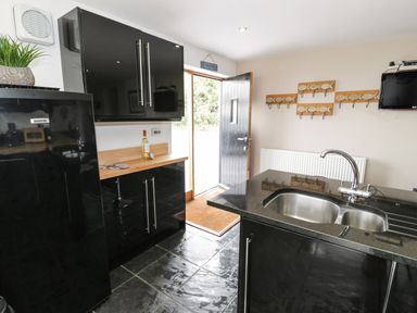 A kitchen with black cabinets a sink and a door leading outside at Bwthyn Awel in Church Bay near Cemaes Bay