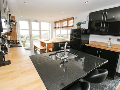 A kitchen with wooden counters black cabinets black island with sink and stools and a wooden dining area with bench seating at Bwthyn Awel in Church Bay near Cemaes Bay