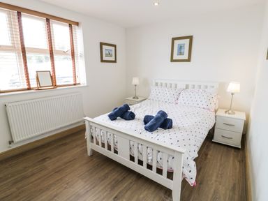 A bedroom with a white bed frame blue towels on the bed bedside tables with lamps and framed pictures on the walls at Bwthyn Awel in Church Bay near Cemaes Bay