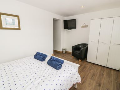 A bedroom with a bed with blue towels on it a black chair a white wardrobe and a wall-mounted TV at Bwthyn Awel in Church Bay near Cemaes Bay