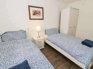 A bedroom with two single beds a nightstand with lamp a wardrobe and framed picture on wall at Bwthyn Awel in Church Bay near Cemaes Bay