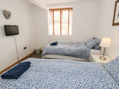 A bedroom with two single beds with blue patterned bedding a bedside table with a lamp and a wall-mounted tv at Bwthyn Awel Church Bay near Cemaes Bay