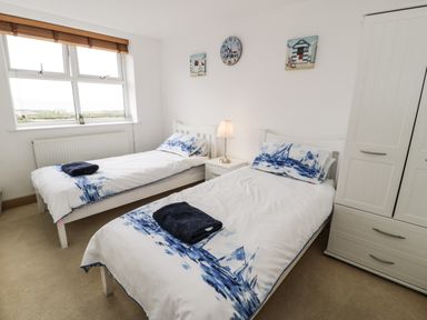 A bedroom with two single beds a nightstand with a lamp a wardrobe and wall decorations at Bwthyn Awel in Church Bay near Cemaes Bay