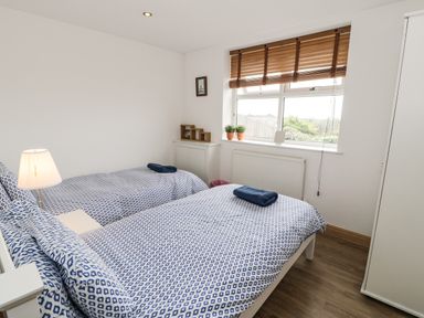A bedroom with two single beds with patterned bedding and a window with blinds at Bwthyn Awel in Church Bay near Cemaes Bay