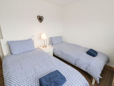 A bedroom with two single beds with blue patterned bedding and a nightstand with a lamp between at Bwthyn Awel in Church Bay near Cemaes Bay