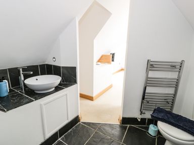 A bathroom with a round basin on a black tiled counter and a metal towel rack at Bwthyn Awel in Church Bay near Cemaes Bay