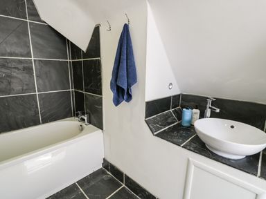 A bathroom with a bathtub blue towel hanging and a round sink on a black tiled counter at Bwthyn Awel in Church Bay near Cemaes Bay