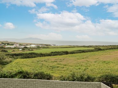A coastal landscape with fields bushes and buildings near the sea at Bwthyn Awel Church Bay near Cemaes Bay