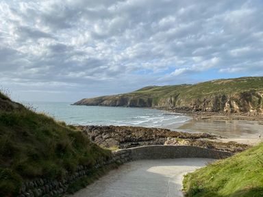 A coastal path leading to a sandy beach with cliffs and grassy hills at Bwthyn Awel Church Bay near Cemaes Bay