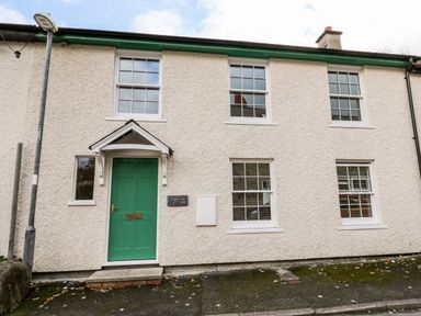 The exterior of a white textured house with a green door and multiple windows at Bridgend Cottages in Howey near Llandrindod Wells