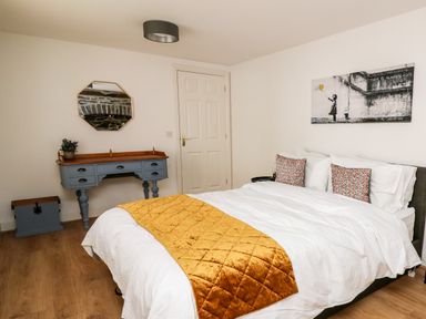 A bedroom with a bed with white bedding and orange throw pillows and blanket a blue dresser with a mirror and a door Bridgend Cottages Howey near Llandrindod Wells