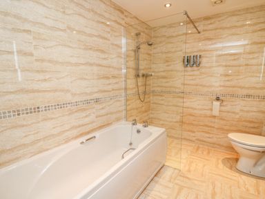 A bathroom with a bathtub shower combination a toilet and tiled walls and floor at Bridgend Cottages in Howey near Llandrindod Wells