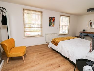 A bedroom with a bed a yellow chair two windows with blinds a blue desk and a mirror at Bridgend Cottages in Howey near Llandrindod Wells