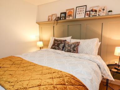 A bed with white patterned bedding and brown pillows with a yellow throw and framed pictures above the headboard at Bridgend Cottages in Howey near Llandrindod Wells