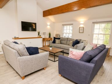 A living room with three sofas a wooden coffee table a wall-mounted TV and wooden beams at Bridgend Cottages in Howey near Llandrindod Wells