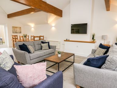 A living room with two gray sofas a blue armchair a wooden coffee table and a mounted TV at Bridgend Cottages in Howey near Llandrindod Wells