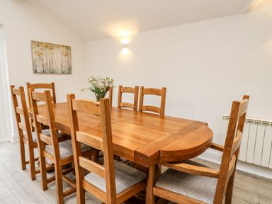 A dining room with a wooden table and eight chairs with a flower vase on the table at Bridgend Cottages in Howey near Llandrindod Wells