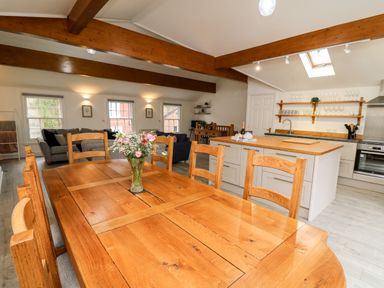 A dining area with a wooden table and chairs and a vase of flowers next to a kitchen with an island and open shelves at Bridgend Cottages Howey near Llandrindod Wells