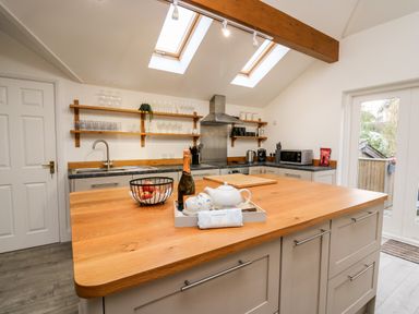 A kitchen with wooden island countertop glasses on wall shelves and a door leading outside at Bridgend Cottages in Howey near Llandrindod Wells