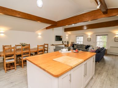 An open-plan kitchen and living area with a wooden countertop island dining table with chairs and sofas at Bridgend Cottages in Howey near Llandrindod Wells