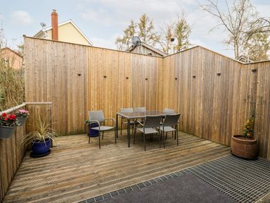 An outdoor wooden deck with a dining table and six chairs surrounded by wooden fences and potted plants at Bridgend Cottages in Howey near Llandrindod Wells