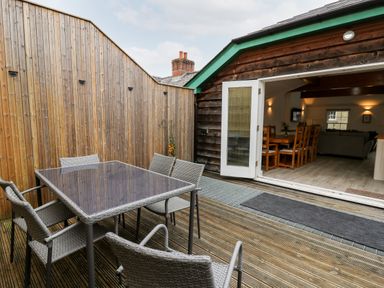 An outdoor patio with a glass table and six chairs next to an open door leading to a dining room at Bridgend Cottages in Howey near Llandrindod Wells