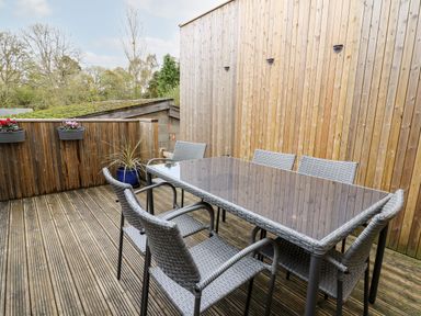 An outdoor wooden deck area with a glass table and six wicker chairs at Bridgend Cottages in Howey near Llandrindod Wells