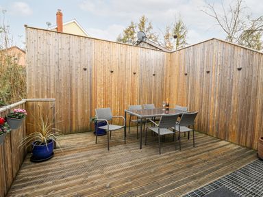 An outdoor patio with wooden decking a glass table six chairs and several potted plants at Bridgend Cottages in Howey near Llandrindod Wells