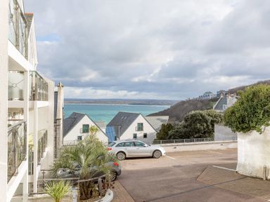 A parking area with two cars near white houses and a view of the sea at The Waves in St Ives
