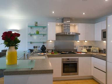 A kitchen with white cabinets a stove a kettle toaster and flowers on the counter at The Waves in St Ives