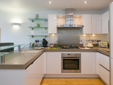 A kitchen with white cabinets a stove oven toaster kettle and glass shelves at The Waves in St Ives