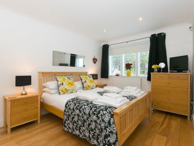 A bedroom with a wooden bed and matching furniture with towels on the bed and flowers on the window at The Waves in St Ives