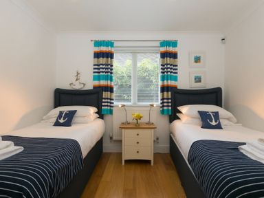 A bedroom with two single beds a nightstand with lamps and flowers and a window with striped curtains at The Waves in St Ives