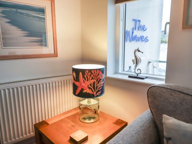 A table lamp with a starfish design on a wooden side table next to a window with a seahorse decoration at The Waves in St Ives