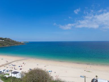 A sandy beach with people and umbrellas by a blue ocean under a clear sky at Turquarze in Carbis Bay