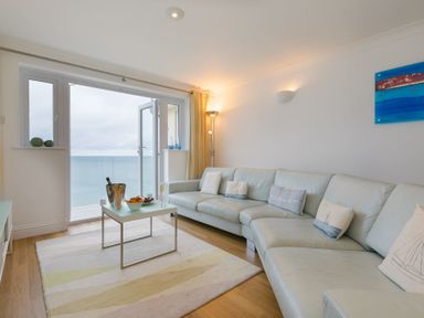 A living room with a large sofa coffee table and an open door leading to a balcony with a sea view at Turquarze in Carbis Bay
