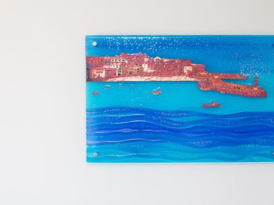 A wall-mounted rectangular artwork depicting a coastal town with buildings a harbor and a lighthouse over blue waves at Turquarze in Carbis Bay