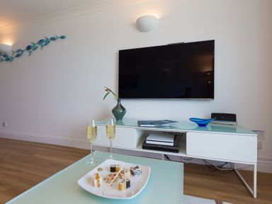 A living room with a wall mounted television white entertainment unit sushi and two glasses on a table at Turquarze in Carbis Bay