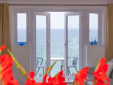 An indoor space with a seating area and open double doors leading to a balcony overlooking the ocean at Turquarze in Carbis Bay