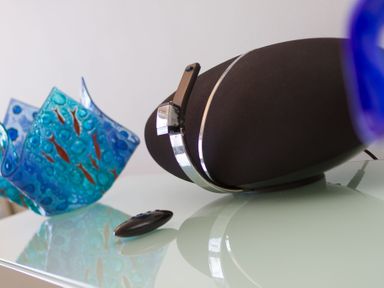 A black speaker with a remote control and a blue decorative glass bowl on a glass surface at Turquarze in Carbis Bay