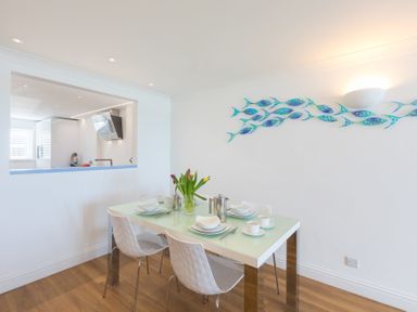 A dining area with a glass table set for four with white chairs and a wall decoration of blue fish at Turquarze in Carbis Bay