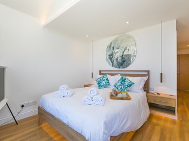 A bedroom with a wooden bed with white bedding and rolled towels on it with two wooden bedside tables and pendant lights at Turquarze in Carbis Bay