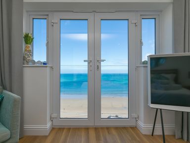 A room with glass doors opening to a beach view with a vase with flowers on the left and a television on the right at Turquarze Carbis Bay