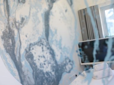 A television on a white table with rolled towels in a room with curtains and a window at Turquarze Carbis Bay